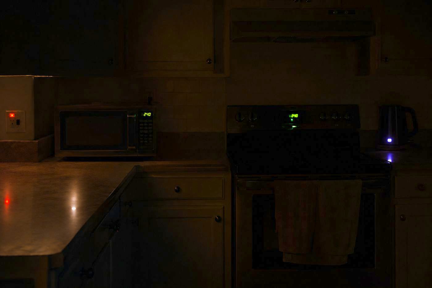 A dark kitchen at night lit only by the standby lights of its appliances