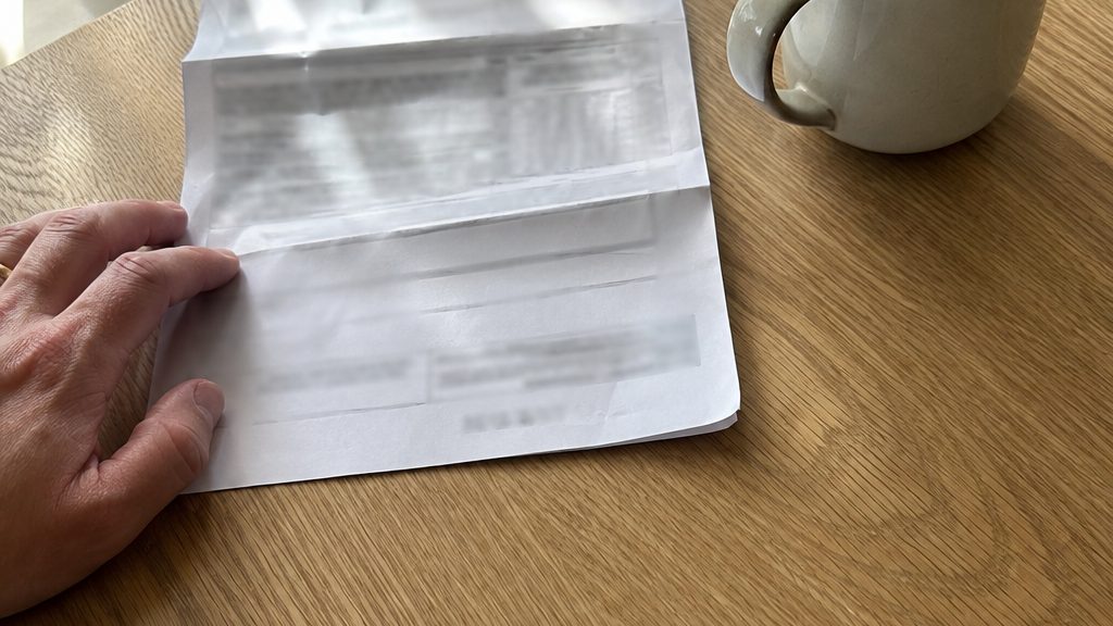 A hand on an electricity bill on a kitchen table next to a cup of coffee