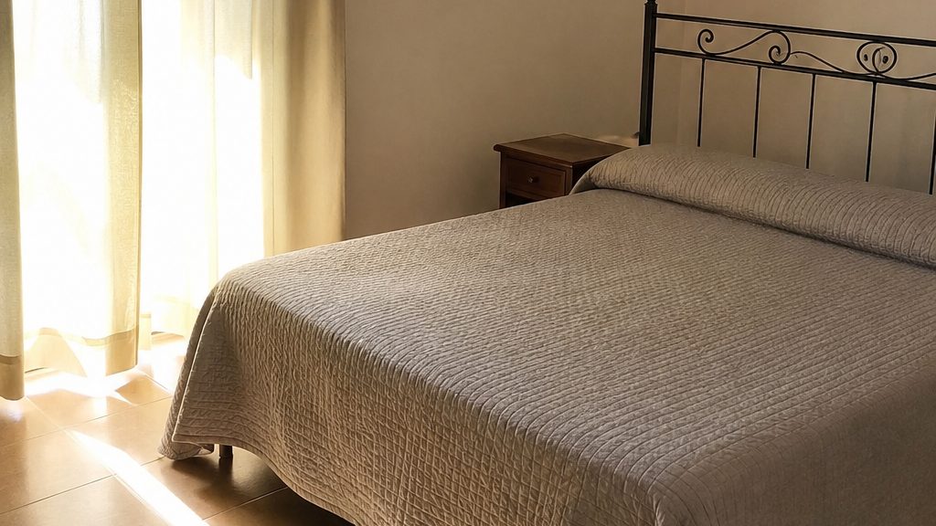 A made bed in an empty rented flat with sun through the curtains